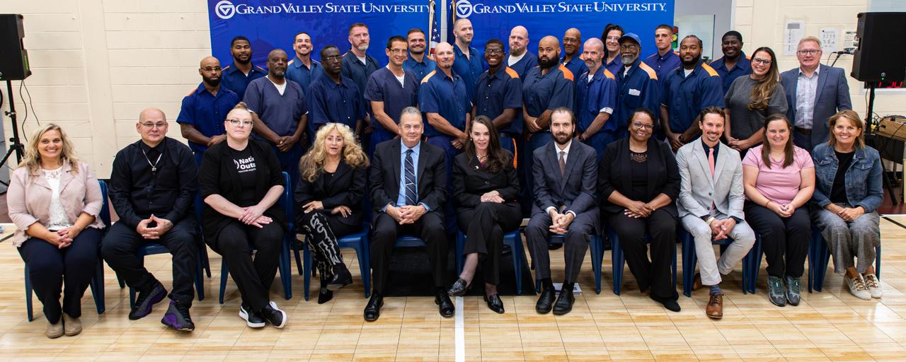 Students, faculty, and staff of the Bellamy Creek Program and Bellamy Creek Correctional Facility seated and standing in front of a backdrop
